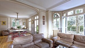 Un salón amplio con sofás de cuero, una zona de comedor con mesa y sillas, y ventanas grandes que ofrecen vistas al exterior.