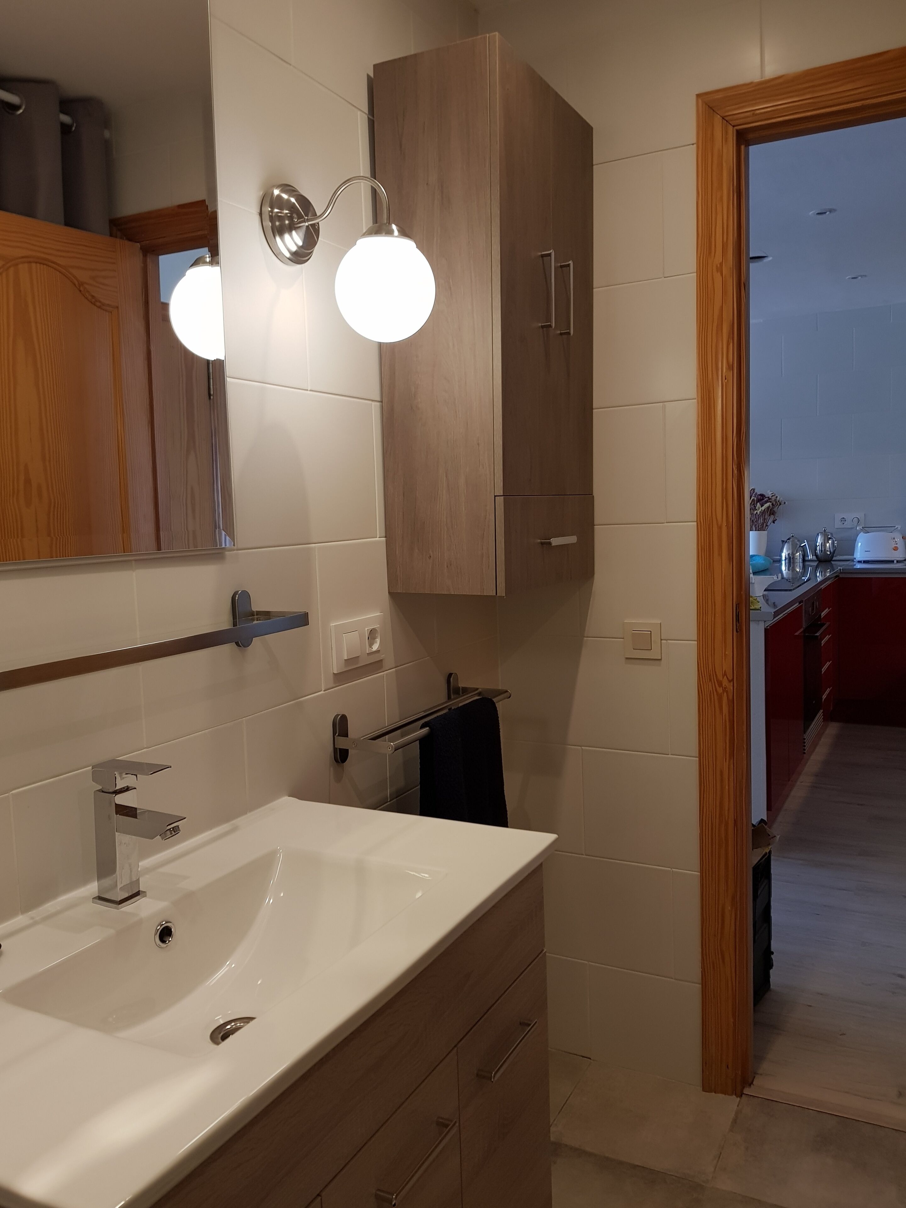 A bathroom with a white sink, wooden cabinets, a towel rack, and a mirror with wall-mounted lights.
