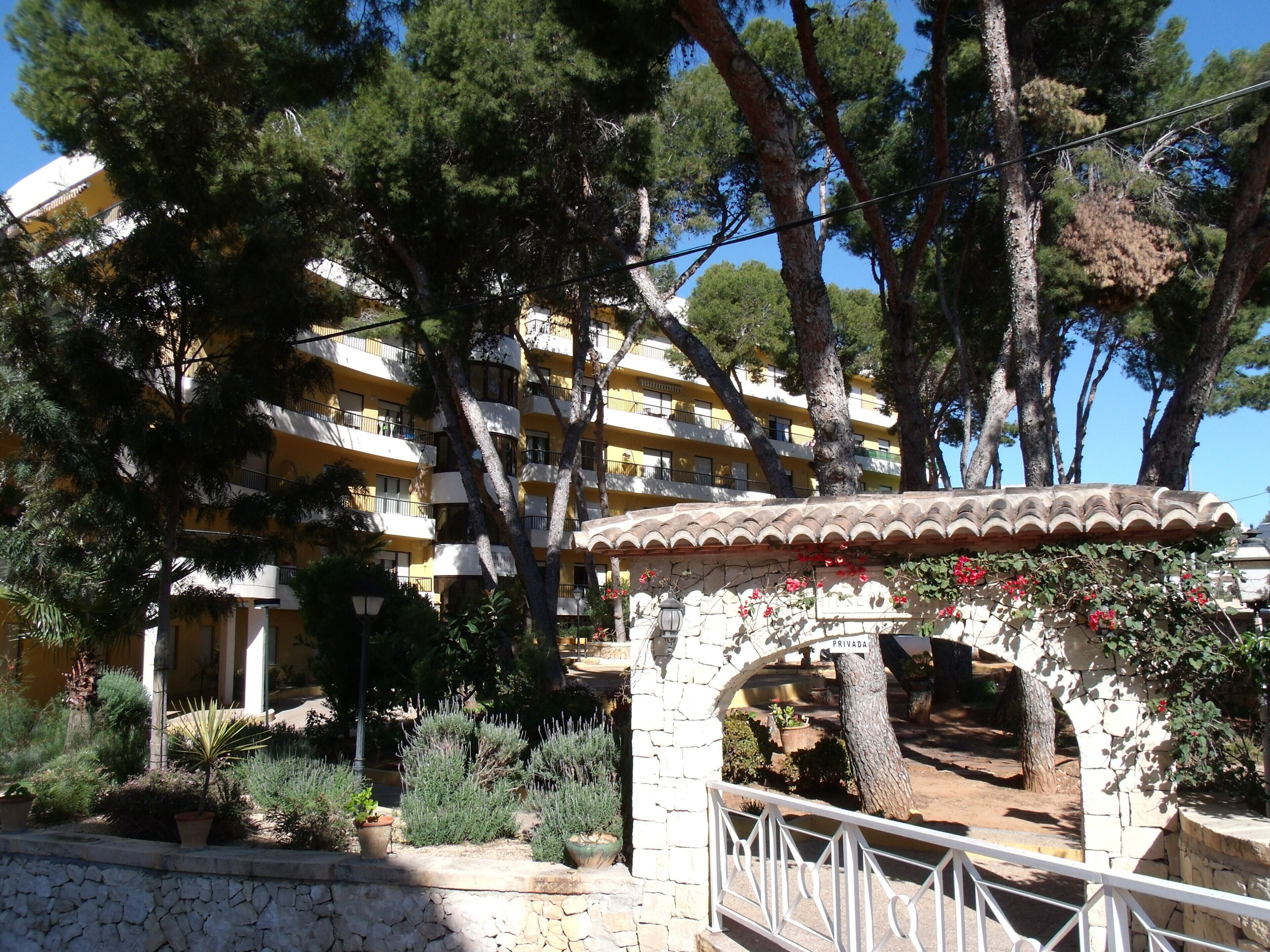 A multi-story building with balconies, surrounded by trees and a stone pathway.