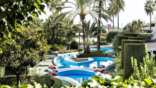 Ein angelegter Garten mit mehreren Pools, Palmen und gepflegten Hecken.