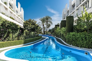 A swimming pool with a curved design, surrounded by lush greenery and modern buildings.