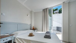 Ein Schlafzimmer mit Bett, Nachttisch, einem Fenster mit Vorhängen und Blick ins Freie.