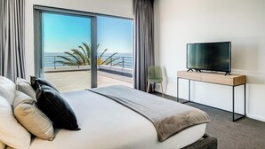 Ein Hotelzimmer mit einem großen Bett, einem Flachbildfernseher auf einem Standfuß und einem Balkon mit Meerblick.