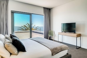 Habitación de hotel con una cama grande, un televisor de pantalla plana sobre un mueble bajo y un balcón con vista al océano.