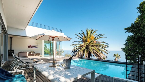 Ein Poolbereich mit Liegestühlen, einem Tisch mit Flasche und Gläsern sowie Blick auf das Meer.