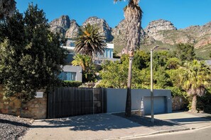 A modern building with a gated entrance, surrounded by lush greenery and mountains in the background. - Incredible Luxury Villa w Ocean Vistas The Views (Cape Town)