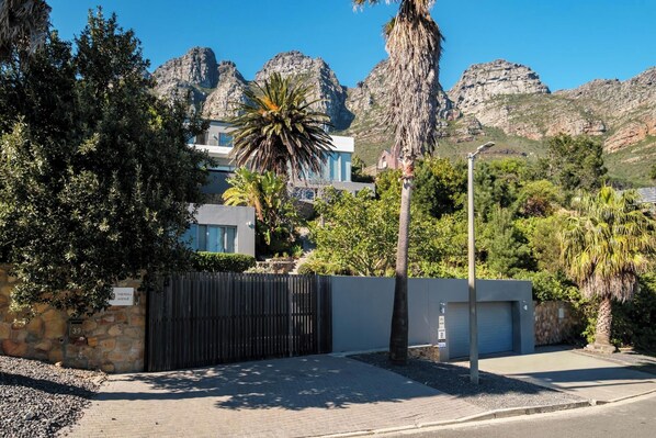 A modern building with a gated entrance, surrounded by lush greenery and mountains in the background. - Incredible Luxury Villa w Ocean Vistas The Views (Cape Town)