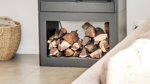 Ein moderner Holzofen mit Glasfront, Korb und Holzvorrat.