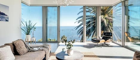 A modern living room with a large window overlooking the sea, a sofa, a coffee table, and a chair.