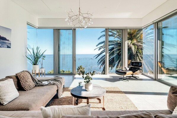 A modern living room with a large window overlooking the sea, a sofa, a coffee table, and a chair.