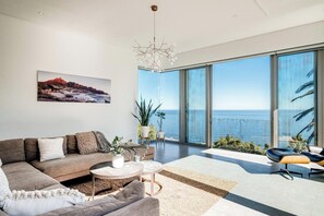 Una sala de estar moderna con un amplio ventanal con vista al océano, un sofá, una mesa de centro y palmeras.