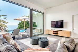 Una sala de estar moderna con un televisor grande, asientos cómodos y vista al océano.