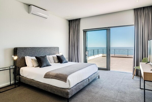 A modern hotel room with a large bed, a desk, and a view of the sea. - Incredible Luxury Villa w Ocean Vistas The Views (Cape Town)