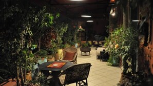 Un patio interior con mesa y sillas, rodeado de plantas en macetas y un suelo de baldosas.