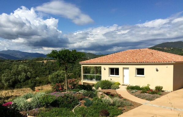 A single-story house with a tiled roof, surrounded by a landscaped garden with various plants and flowers.