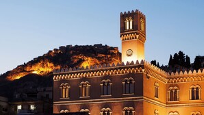Un edificio histórico con una torre destacada y ventanas arqueadas, frente a un paisaje montañoso.