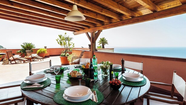 Una mesa de madera preparada para comer, con platos, vasos y cubiertos, con vistas a un paisaje pintoresco.