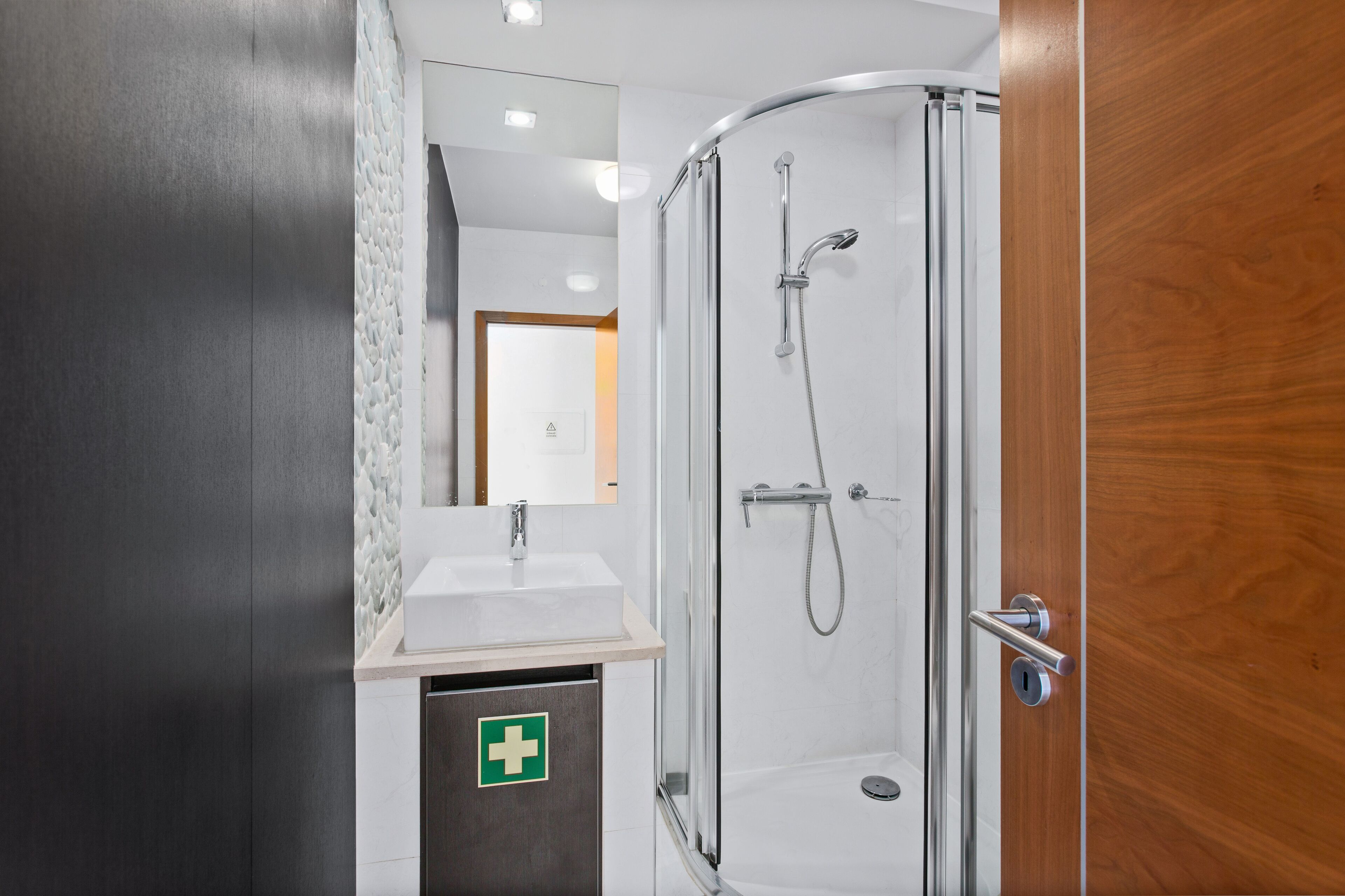 A modern bathroom with a glass-enclosed shower, a sink with a mirror, and a wooden door.