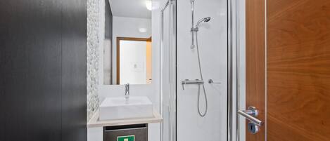 A modern bathroom with a glass-enclosed shower, a sink with a mirror, and a wooden door.