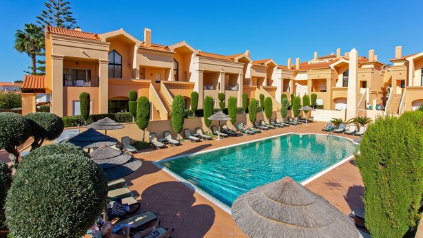 Un resort con piscina, tumbonas y un cielo azul despejado.