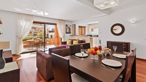 Un comedor moderno con una mesa de madera dispuesta para dos personas, un frutero y una copa de vino.