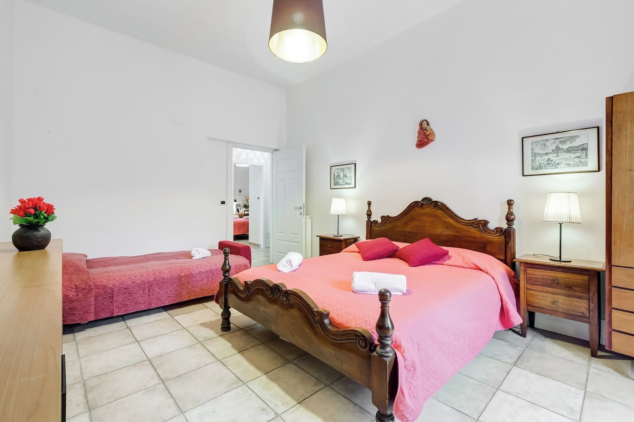 Ein Schlafzimmer mit einem hölzernen Bett, einem Nachttisch mit Lampe, einem roten Sofa und einem Blumenstrauß.