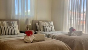 Hotellihuone, jossa on kaksi sänkyä. Jokaisessa sängyssä on raidallinen tyyny, lamppu ja punakukkainen pyyhe.