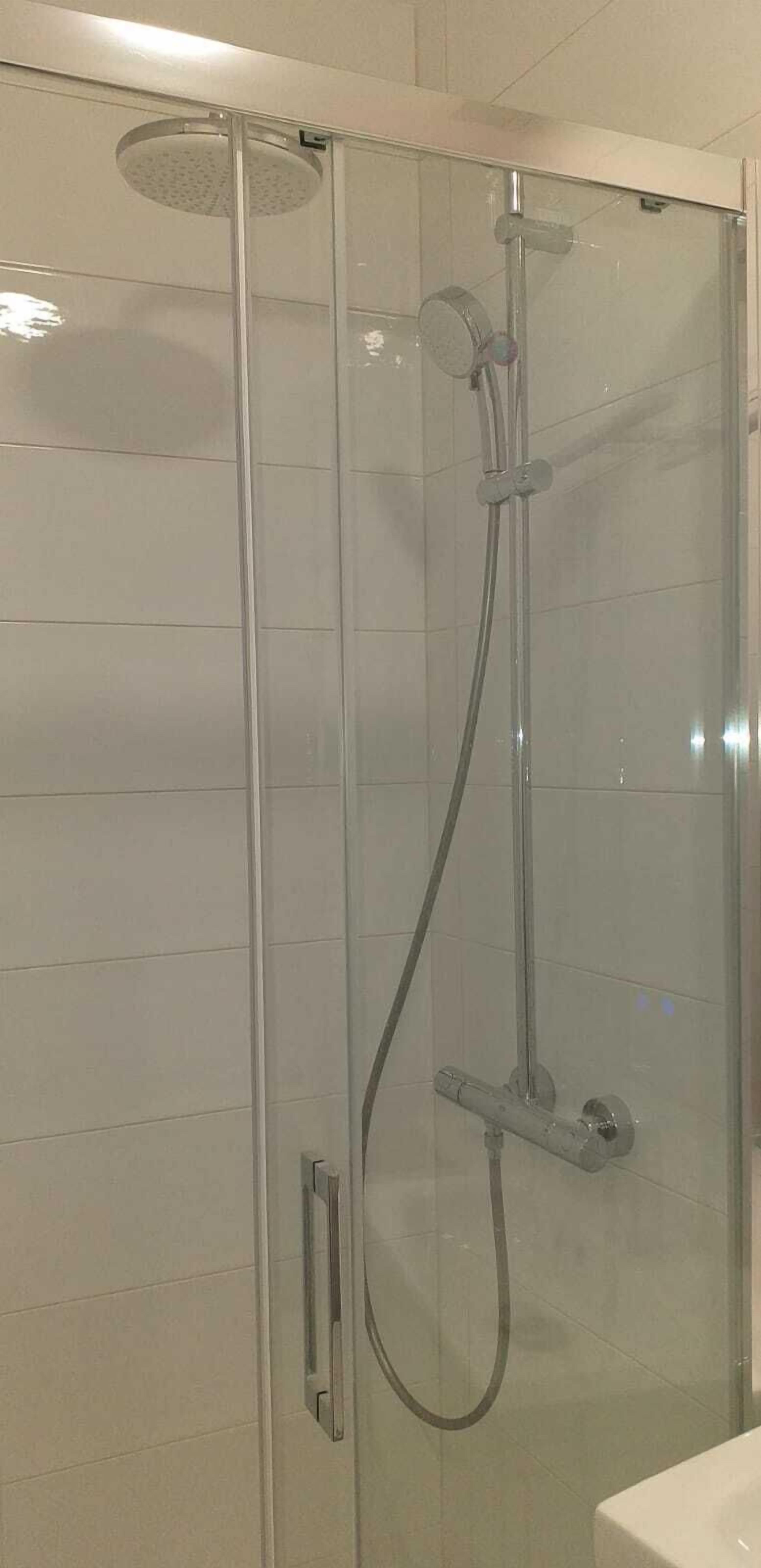 A glass-enclosed shower stall with a handheld showerhead and a wall-mounted faucet.