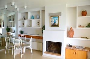 Une cuisine moderne avec des meubles blancs, une table à manger en verre et une cheminée.