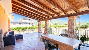 An outdoor patio with a stone column, a table, and chairs, overlooking a vineyard and mountains. - Sa Ingia by All4sardinia (Cardedu)