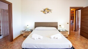 A neatly made bed with white linens, two bedside tables with lamps, and a wall-mounted artwork. - Sa Ingia by All4sardinia (Cardedu)