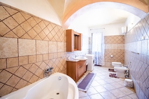 Een badkamer met een vrijstaand bad, een houten wastafelmeubel, een wasmachine en twee toiletten.