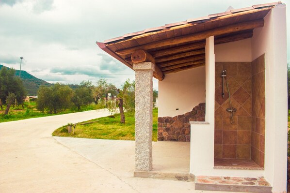 Un área de ducha al aire libre, cubierta, con columnas de piedra y pared de azulejos.