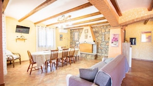 Uma sala de jantar com lareira de pedra, vigas de madeira no teto e televisão fixada na parede.