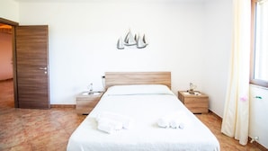 Uma cama bem arrumada com lençóis brancos, duas mesas de cabeceira com luminárias, um painel de cabeceira de madeira e um aplique na parede.