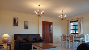 Ein Wohnzimmer mit einer Couch, einem Couchtisch, einem Esstisch mit Stühlen und zwei Kronleuchtern.