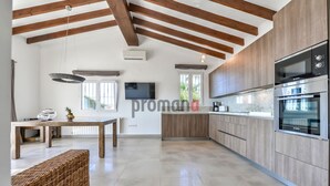 Une cuisine moderne avec des poutres en bois, un coin repas avec une table et des chaises, et un grand téléviseur fixé au mur.