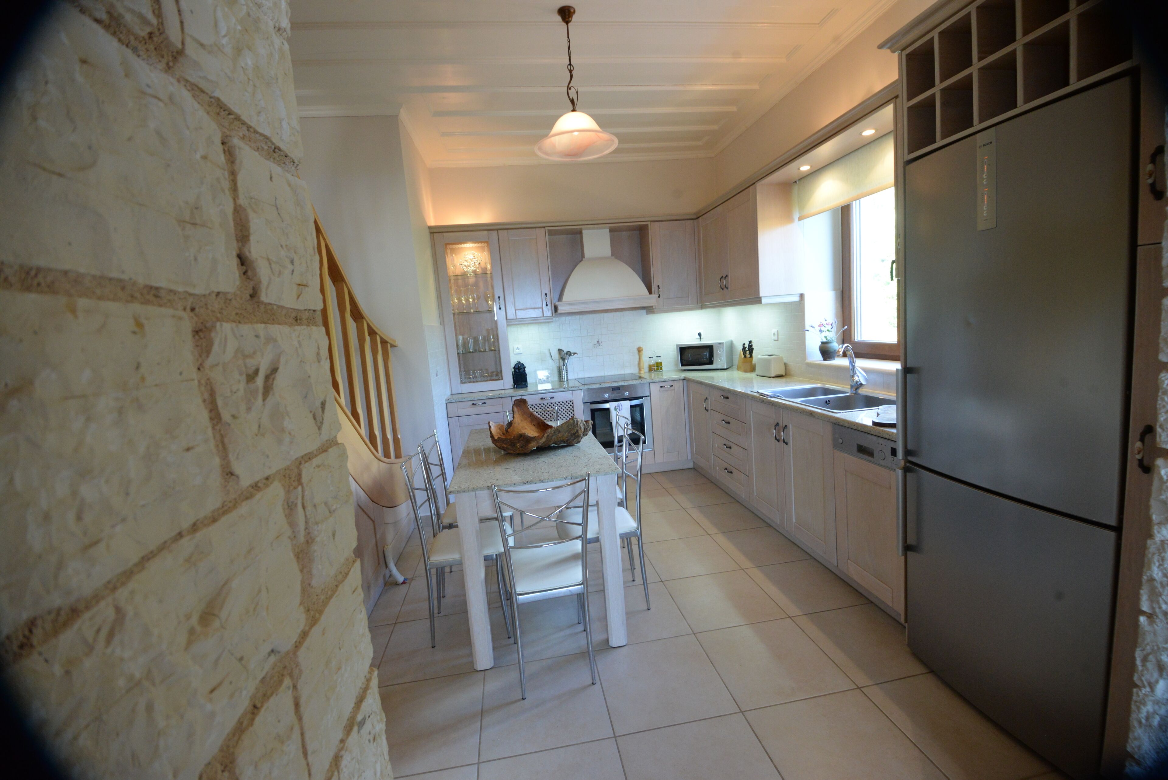 Una cocina con pared de piedra, una mesa de comedor con sillas, un refrigerador y un microondas.