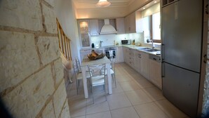 A kitchen with a stone wall, a dining table with chairs, a refrigerator, and a microwave.