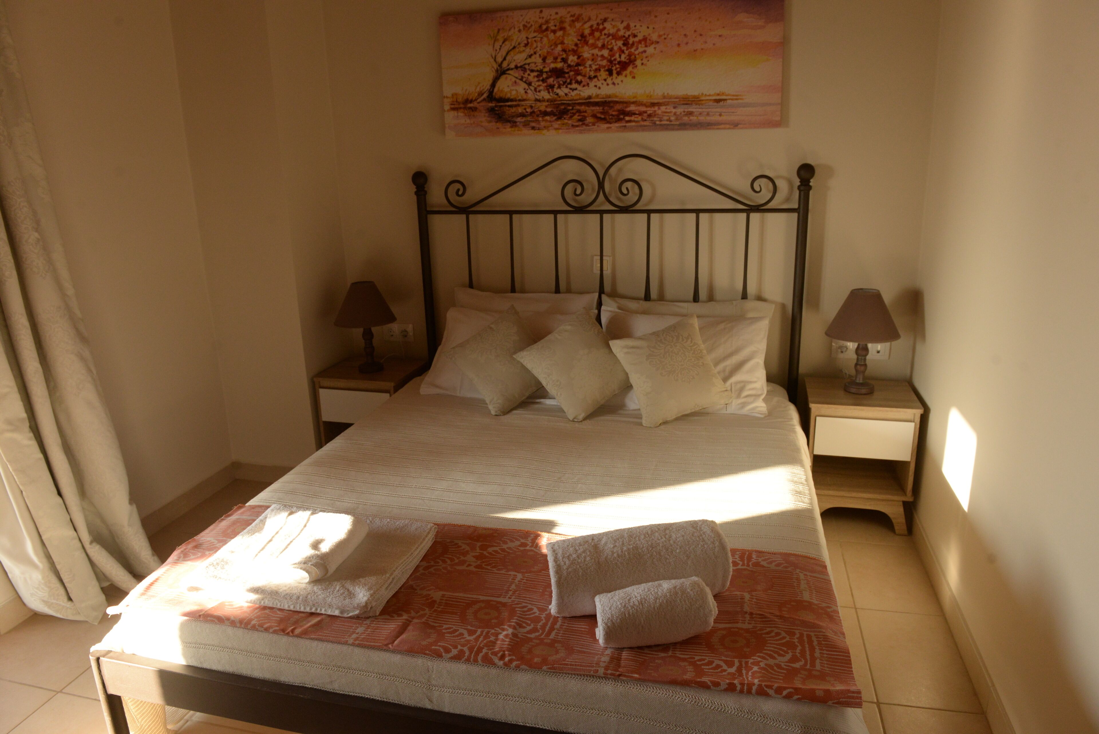 A neatly made bed with pillows and a blanket, two bedside lamps, and a painting on the wall.
