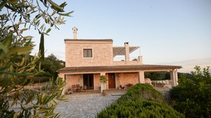 A stone building with a tiled roof, a small window, and a door. There is a paved area in front of the building.