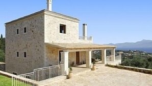 A stone villa with a terrace, a chimney, and a view of the sea.