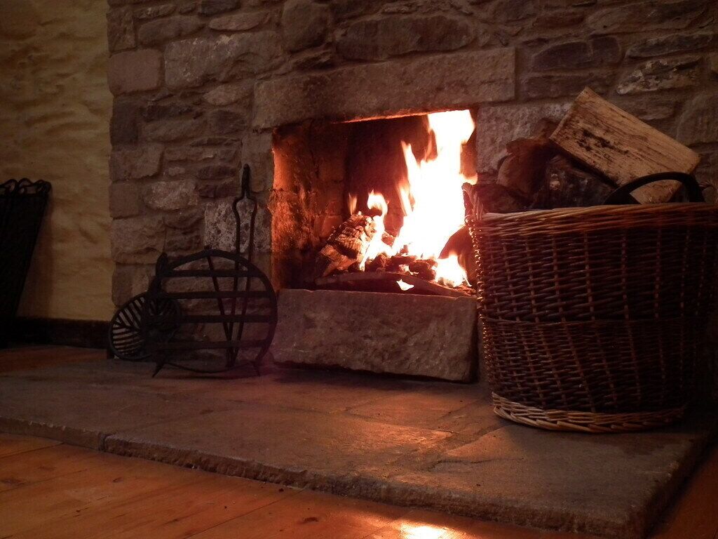 A stone fireplace with a fire burning inside, a wicker basket on the mantel, and a metal basket on the floor.