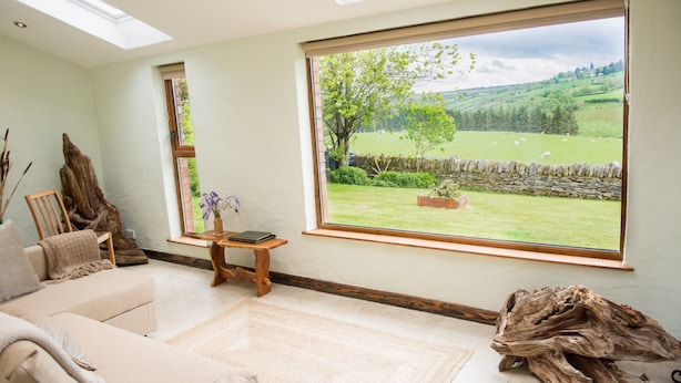 Ein geräumiges Wohnzimmer mit einem großen Fenster, das Blick auf ein grünes Feld und eine Steinmauer bietet.