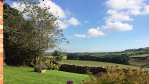 Ein Garten mit Steinmauer, Baum und Blick auf sanfte Hügel.