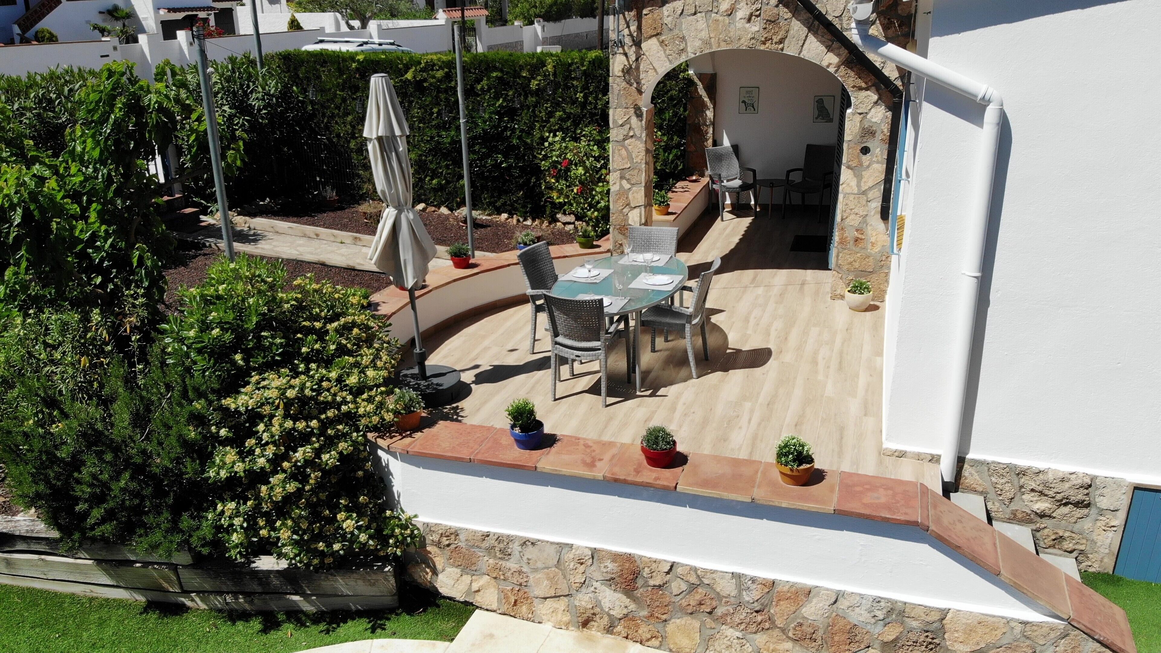 A patio with a table and chairs, surrounded by potted plants and a stone wall.