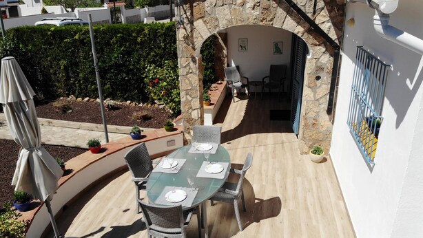 An outdoor dining area with a stone archway, a table set with plates and glasses, and potted plants. - Lovely House - Pool/Garden/Wi-Fi - Casa Palmera (L'Escala)