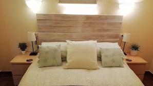A neatly made bed with a wooden headboard, two bedside tables with lamps and small potted plants, and a purple blanket at the foot of the bed. - Lovely House - Pool/Garden/Wi-Fi - Casa Palmera (L'Escala)
