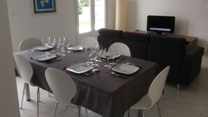A dining area with a table set for six, a sofa, a television, and a window with a view of greenery. - 3-bedroom house near Colmar (Bennwihr)