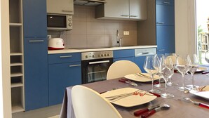 A modern kitchen with blue cabinets, a microwave, an oven, and a dining area set for a meal. - 3-bedroom house near Colmar (Bennwihr)